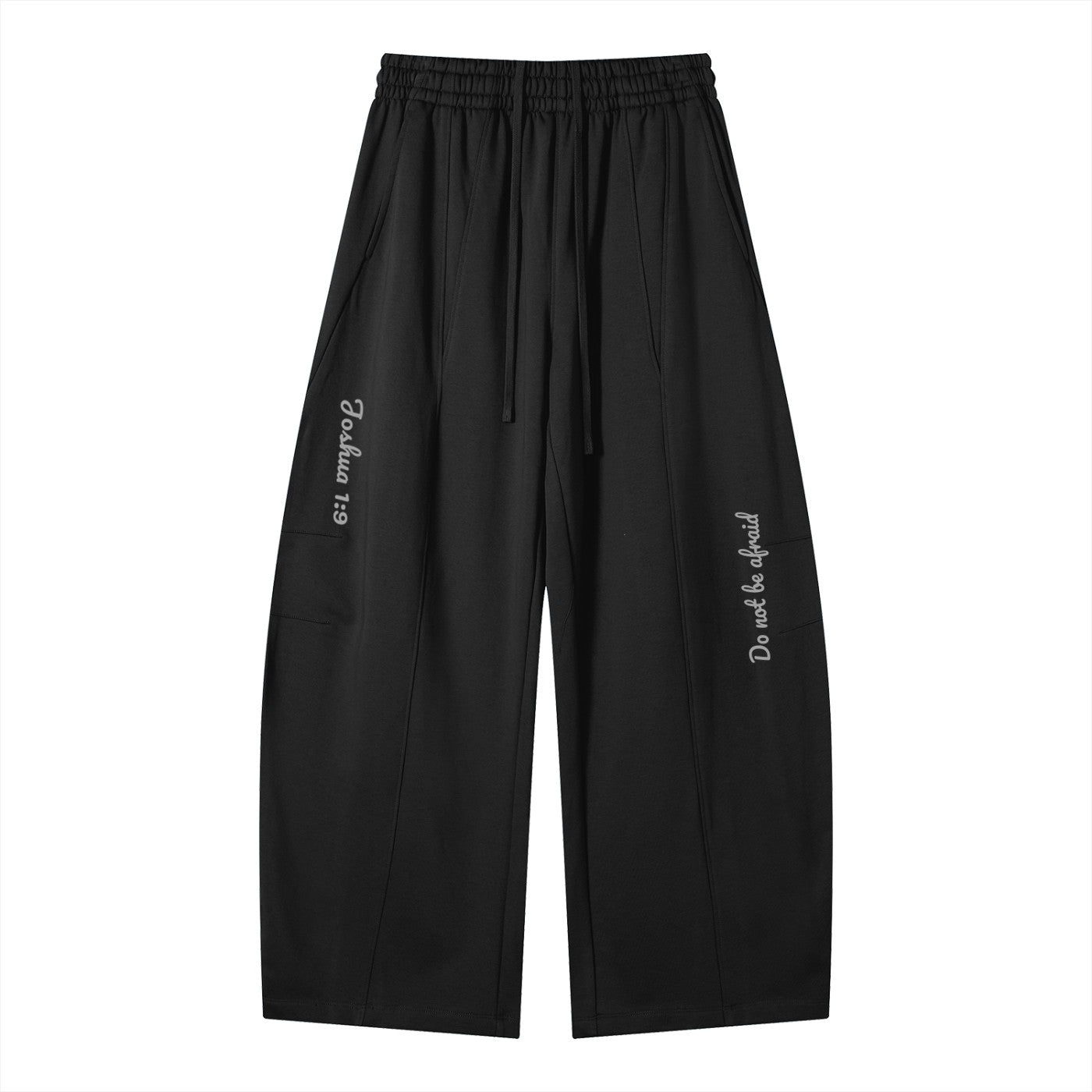 Greater Good black cotton blend wide-leg sweatpants with drawstring, elastic waist, and side pockets. Features text print "Joshua 1:9" on left leg and "Do not be afraid" on right leg.